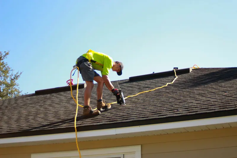 Roofer in a safety harness working on asphalt shingles